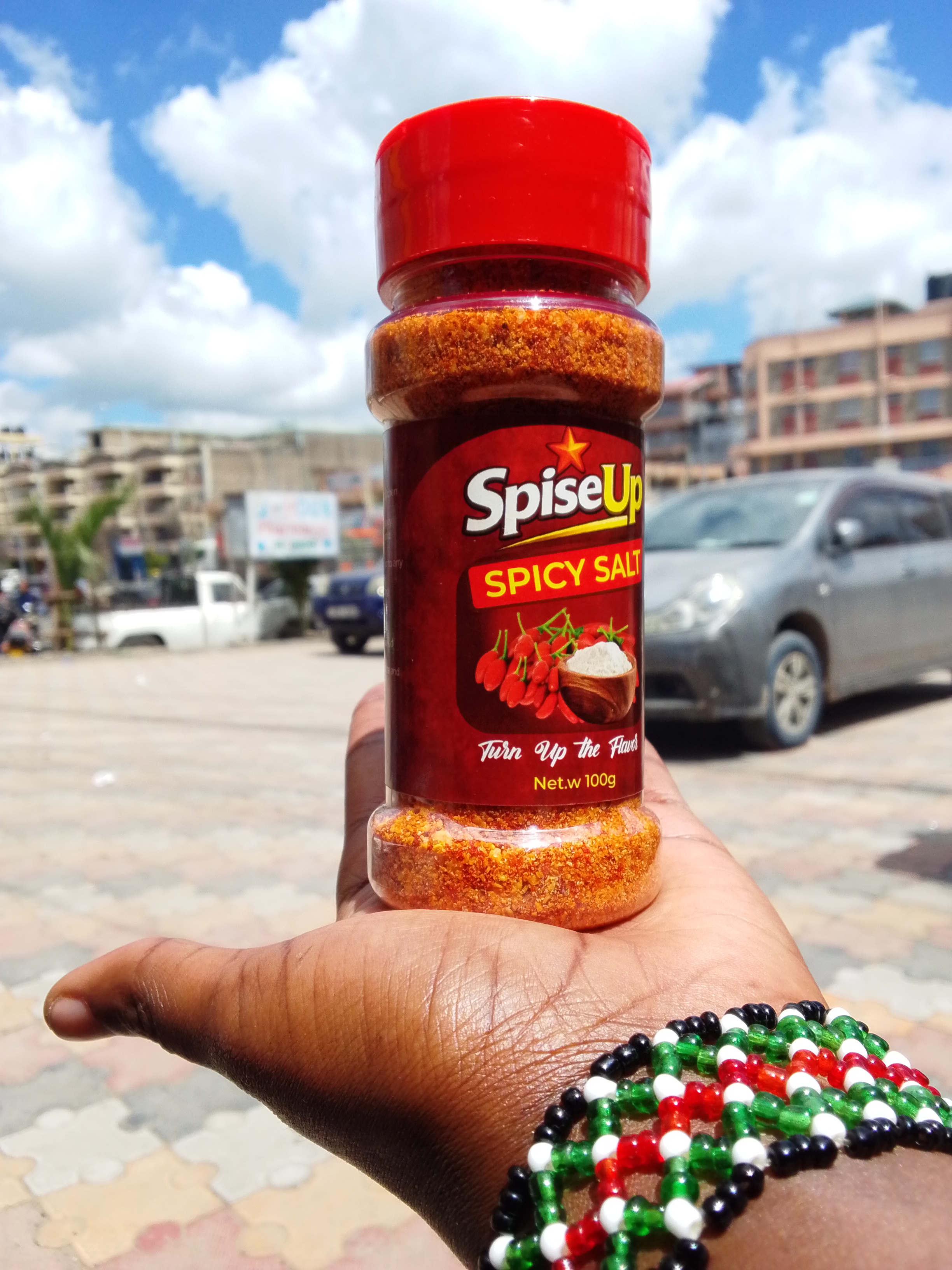 A hand holding a SpiseUp Spicy Salt bottle out on the streets of Kitengela